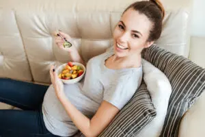 Pregnant woman eating fruit salad on couch 