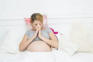 pregnant woman sneezing in bed due to allergies