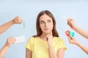 Woman wearing yellow shirt, hands holding up different methods of birth control 